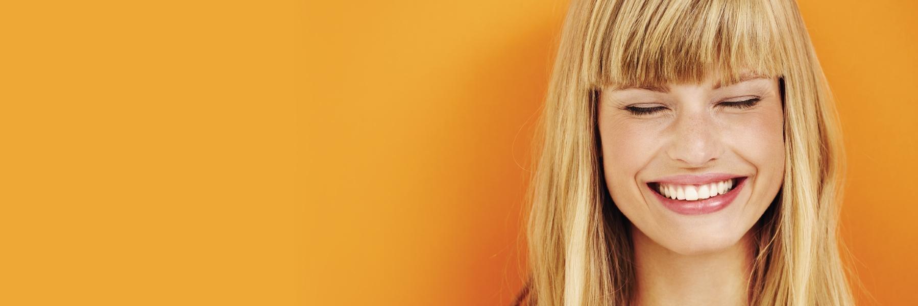 Woman smiling against an orange wall in Greeley, CO